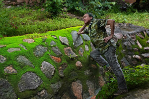 Patrick Blanc leaning on a stone wall covered with green iridescent mosses, Lupita island, Kipili, Lake Tanganyika, Tanzania, Jan. 2021